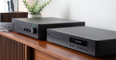 Amplificateur intégré NAD C 359S et lecteur CD NAD C 569 noirs posés côte à côte sur un meuble en bois, afficheur du lecteur allumé