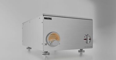 Amplificateur de puissance stéréo Nagra AMP II-S en aluminium brossé argent vu de trois quarts, avec Modulomètre à aiguille rétroéclairé et sélecteur rotatif en façade, posé sur pieds découplés