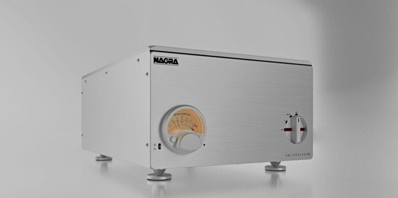 Amplificateur de puissance stéréo Nagra AMP II-S en aluminium brossé argent vu de trois quarts, avec Modulomètre à aiguille rétroéclairé et sélecteur rotatif en façade, posé sur pieds découplés