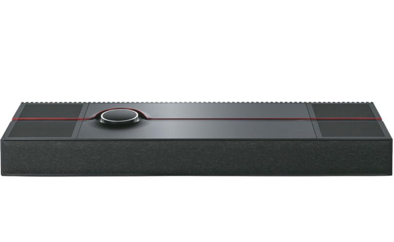 Système tout-en-un Naim Mu-so Utopia vu de trois quarts dessus, coffret noir d'un mètre de large à grilles rainurées, liseré rouge et molette de commande rétroéclairée