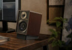 Enceinte active Onkyo GX-30ARC édition 80 ans en finition noyer Bordeaux, façade noire texturée et cerclages gris foncé, posée sur son pied incliné noir au coin d'un bureau en bois