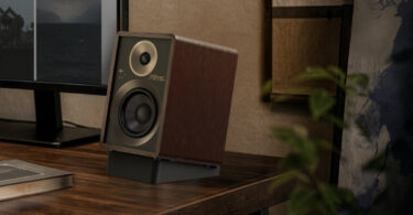 Enceinte active Onkyo GX-30ARC édition 80 ans en finition noyer Bordeaux, façade noire texturée et cerclages gris foncé, posée sur son pied incliné noir au coin d'un bureau en bois