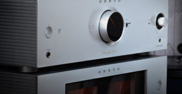 Préampli réseau Onkyo Icon P-80 argent posé sur l'ampli de puissance M-80 et ses deux vumètres, vus de trois quarts dans un salon à côté d'une platine vinyle