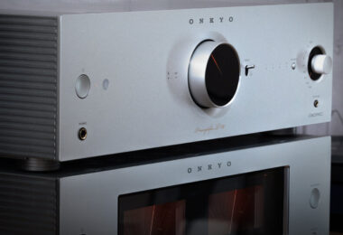 Préampli réseau Onkyo Icon P-80 argent posé sur l'ampli de puissance M-80 et ses deux vumètres, vus de trois quarts dans un salon à côté d'une platine vinyle