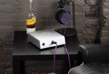 Ampli casque Orchard Audio Valencia en finition argent posé sur un meuble noir, câble de casque violet branché en façade, casque sur son support devant un mur de briques