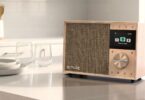 Radio Pure Evoke One en bois de bouleau posée sur un plan de travail de cuisine, grille en tissu, écran couleur affichant le menu radio Internet, molette en métal et touches de présélection