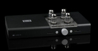 réamplificateur symétrique Schiit Freya 2 en finition noire, vu de trois quarts, avec ses quatre lampes octales émergeant de la grille ajourée du capot, son bouton de volume central argenté et ses deux afficheurs en façade