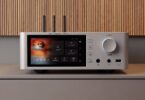 Shanling SM1.3R HD en finition argent posé sur un meuble, avec son écran tactile 2K de 5,98 pouces, ses trois antennes Wi-Fi et Bluetooth, son bouton de volume rétroéclairé et ses sorties casque en façade