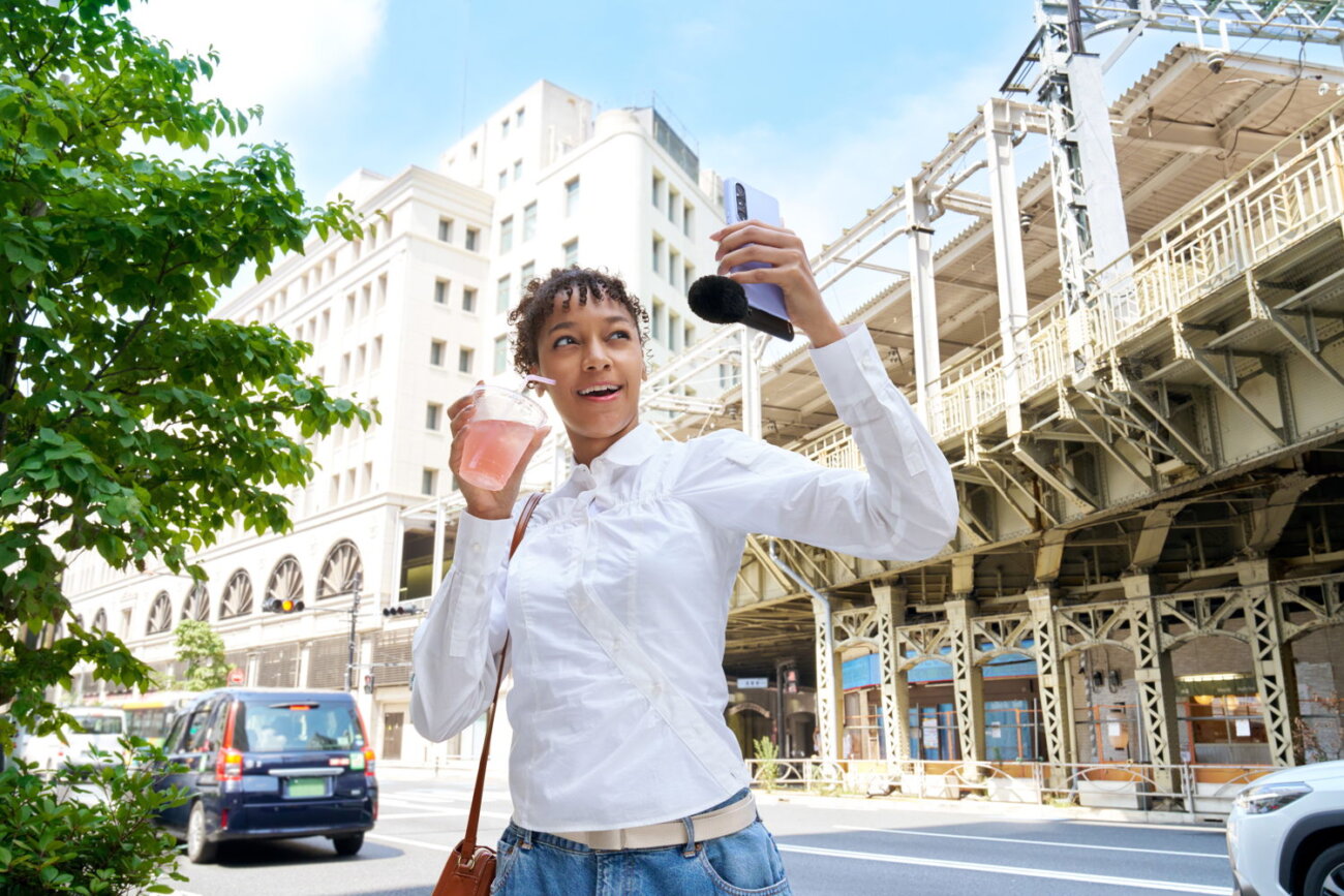 Jeune femme filmant un selfie en ville avec un smartphone équipé du micro Sony ECM-AX10 et de sa bonnette anti-vent en fourrure noire, caméra frontale orientée vers elle