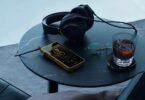 Baladeur Sony Walkman NW-WM1ZM3 à châssis en cuivre sans oxygène plaqué or posé sur une table avec un casque filaire, écran 5,5 pouces et lecteur de musique affiché