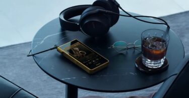 Baladeur Sony Walkman NW-WM1ZM3 à châssis en cuivre sans oxygène plaqué or posé sur une table avec un casque filaire, écran 5,5 pouces et lecteur de musique affiché