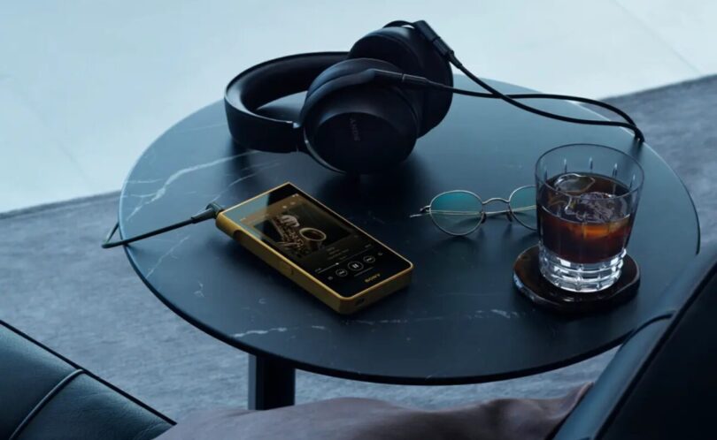 Baladeur Sony Walkman NW-WM1ZM3 à châssis en cuivre sans oxygène plaqué or posé sur une table avec un casque filaire, écran 5,5 pouces et lecteur de musique affiché