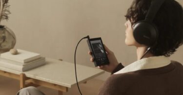 Auditeur assis dans un fauteuil écoutant de la musique au casque Sony sur le baladeur Walkman NW-ZX900 noir à écran 5 pouces Full HD relié par câble