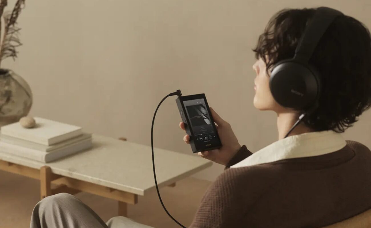 Auditeur assis dans un fauteuil écoutant de la musique au casque Sony sur le baladeur Walkman NW-ZX900 noir à écran 5 pouces Full HD relié par câble