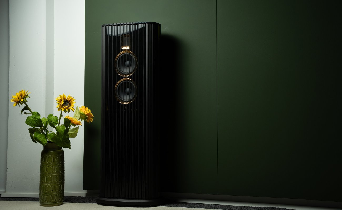 Nouvelle enceinte colonne Steinway & Sons Model O noire laquée avec deux haut-parleurs médium-grave cerclés d'or et tweeter AMT, placée près d'un mur vert