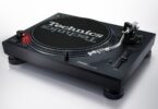 Platine DJ Technics SL-1210MKX noire vue de trois quarts avec plateau, feutrine Technics, bras en S argent poli, curseur de pitch et nouveaux pieds isolants