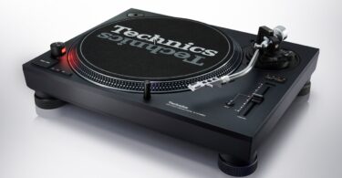 Platine DJ Technics SL-1210MKX noire vue de trois quarts avec plateau, feutrine Technics, bras en S argent poli, curseur de pitch et nouveaux pieds isolants