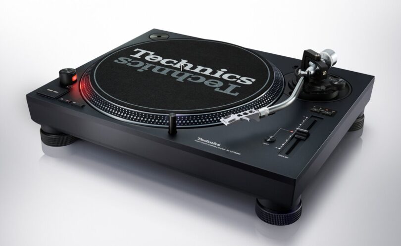 Platine DJ Technics SL-1210MKX noire vue de trois quarts avec plateau, feutrine Technics, bras en S argent poli, curseur de pitch et nouveaux pieds isolants