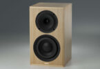 Enceinte active True Tone T1 Signature en finition chêne, sans grille : haut-parleur coaxial en haut et boomer en bas de la façade, sur fond gris