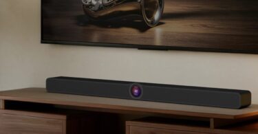 Barre de son WiiM Bar noire posée sur un meuble TV en noyer sous un téléviseur, avec son écran tactile rond de 2,1 pouces au centre de la façade, dans un salon chaleureux