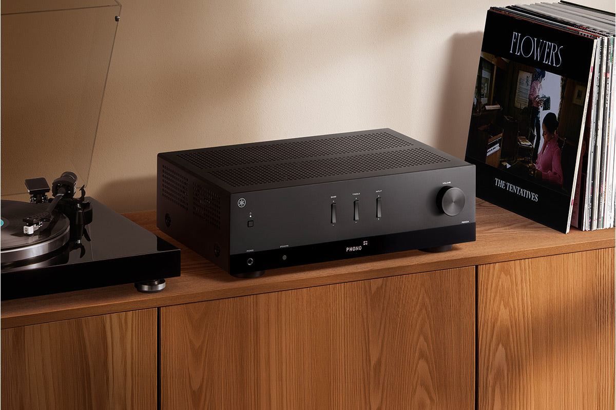 Ampli-tuner Yamaha R200A noir posé sur un meuble en bois à côté d'une platine vinyle et de pochettes de disques